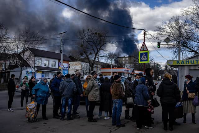 People stand in line in front of a supermarket while smoke billows over the town of Vasylkiv just outside Kyiv on February 27, 2022, after overnight Russian strikes hit an oil depot. Photo by DIMITAR DILKOFF/AFP via Getty Images