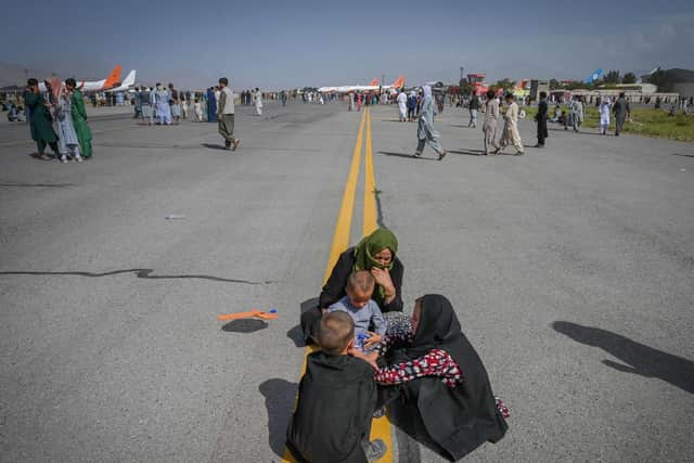 Afghan people sit along the tarmac as they wait to leave Kabul airport after a stunningly swift end to Afghanistan's 20-year war, as thousands of people mobbed the city's airport trying to flee the group's feared hardline brand of Islamist rule. Photo by WAKIL KOHSAR/AFP via Getty Images