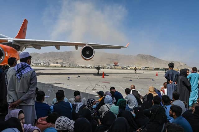 Afghan people sit along the tarmac as they wait to leave Kabul airport after a stunningly swift end to Afghanistan's 20-year war, as thousands of people mobbed the city's airport trying to flee the group's feared hardline brand of Islamist rule. Photo by WAKIL KOHSAR/AFP via Getty Images