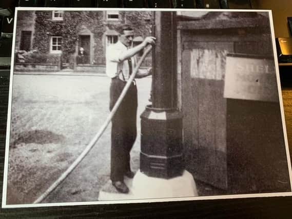 Early 1920s photo of George Lamb using a manual petrol pump at his garage near the fountain at Hornby.