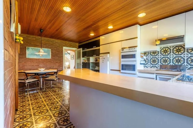 The kitchen is equipped with wall and base units, bound by a large kitchen bar and surrounded by Amtico tiled floors and walls.