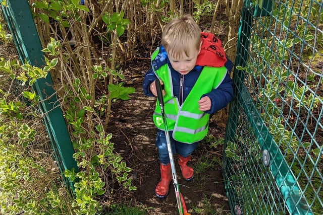 A little boy picks litter in the undergrowth.