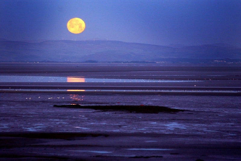 A clear morning sky reveals a setting moon over Morecambe Bay.