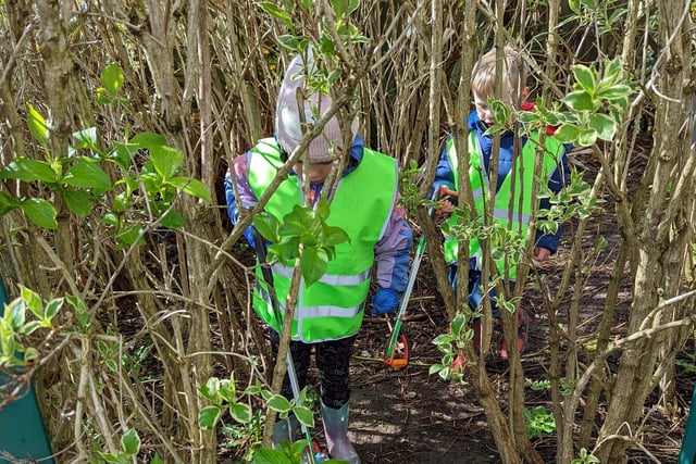 Two children among the undergrowth picking up litter.