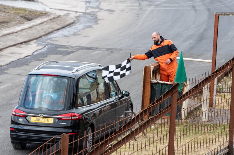 A chequered flag is raised as the hearse carrying the coffin of Gerald Hoggarth circles around the Warton Stock Car track for one last lap. Photo: Kelvin Lister-Stuttard.