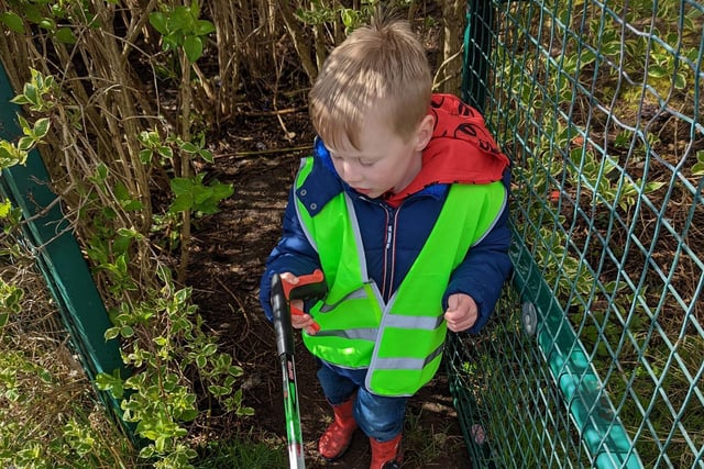 A little boy picks litter in the undergrowth.