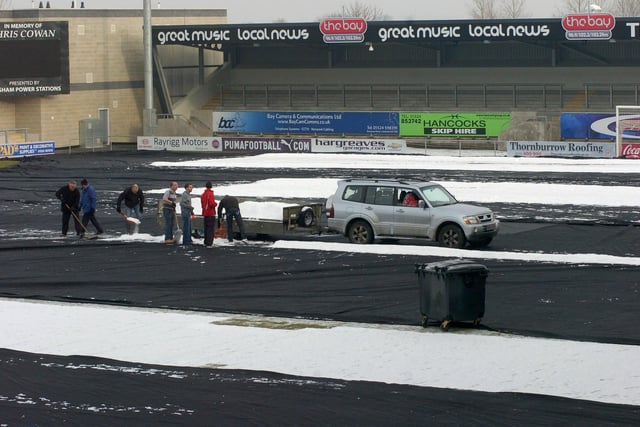 Morecambe fans, groundstaff and club officials help get snow off the covers protecting the pitch at the Globe Arena on Boxing Day in preparation for the fixtures against Aldershot and Accrington Stanley.