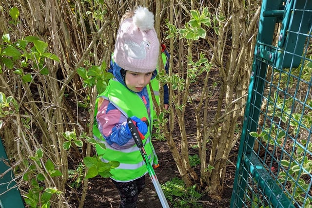 A little girl picks up litter in the undergrowth.