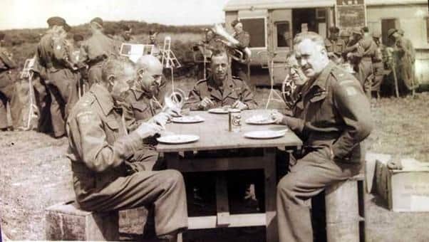 Officers of the 4th (South Lonsdale) Battalion Home Guard having lunch whilst the band prepares for a rehearsal.  The former railway carriage to the rear has been adapted for use by the soldiers.  The photograph appears to be by a Morecambe photographer and may well be at Crag Bank, where it is known the Home Guard trained. Kings Own Museum Accession Number: KO2917/55