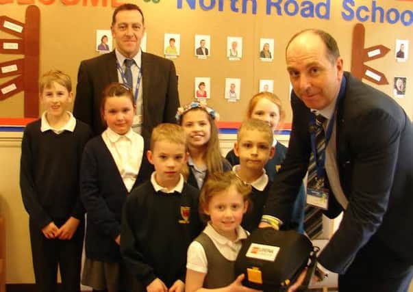 Carnforth North Road School children and head Adrian Ibison are handed the new defibrillator by ADAM Appeal trustee James Mullin.