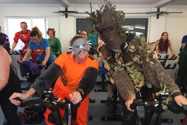 The two spin bikes in front of picture, left to right Lisa Spurr BayFit member (aka Rocket Raccoon!) Ellen Smith Bay Fit member and fundraiser at Unique Kidz and Co (aka Groot!)