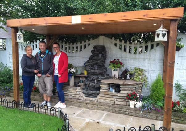 Tony and Julie Wiles with their daughter Louisa next to the memorial water feature in their garden.