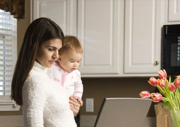 Mother holding baby  and typing on laptop computer in kitchen.